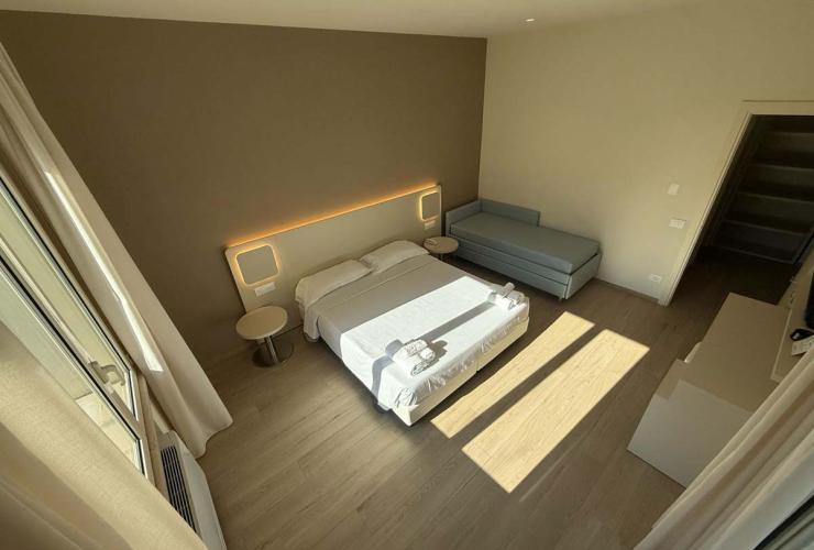 Camera moderna e luminosa, letto matrimoniale, divano, atmosfera accogliente e rilassante.