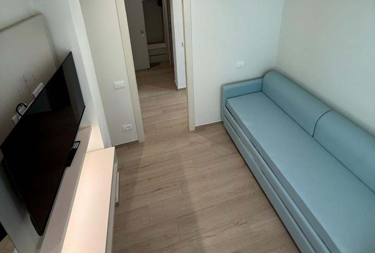 Stanza moderna, luminosa e minimalista con divano azzurro e TV a parete.