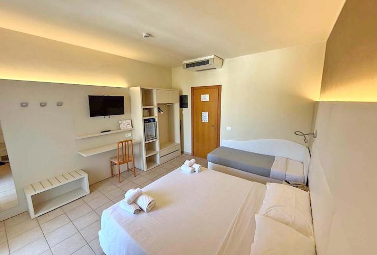 Camera d'albergo luminosa, accogliente, con letto matrimoniale, divano, TV e arredi moderni.