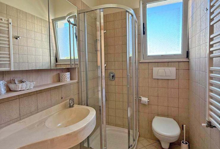 Bagno luminoso, moderno, con doccia, bidet e finestra aperta su cielo azzurro.
